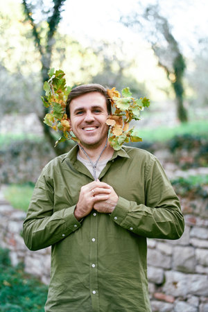 Young smiling man peeks through a yellowing oak branch in his hands in the park