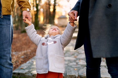 Little girl holds her parents hands with her head up. Cropped