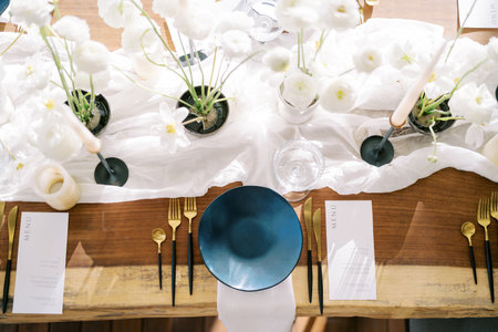 Black plate on a white napkin stands next to gold cutlery and a menu on a holiday table. Top view