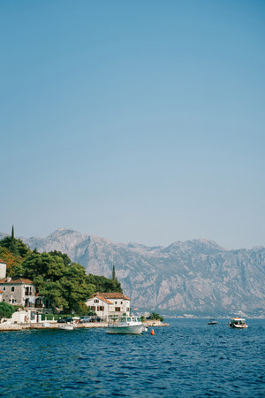 Boats stand off the coast of Perast with old houses among green trees. Montenegro
