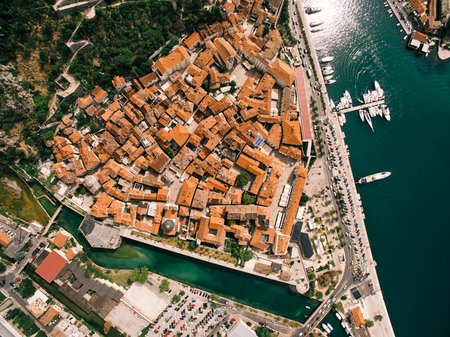 Narrow canal near the fortress walls of the ancient town of Kotor with red roofs on the shore of the...