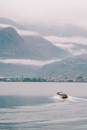 Motor yacht sails on Lake Como towards the mountainous coast in fog. Italyの写真素材