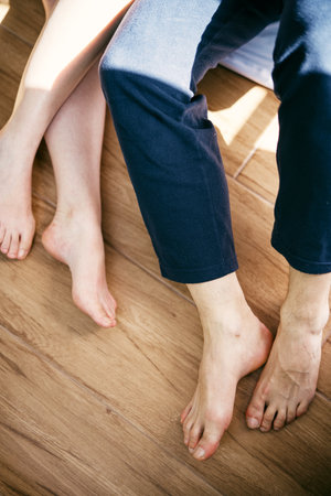 Bare feet of man and woman sitting on a wooden floor. Cropped. Faceless