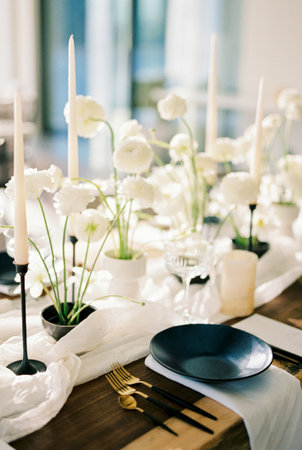 Black plates stand on a wooden table next to white bouquets of flowers on a narrow tableclothの写真素材