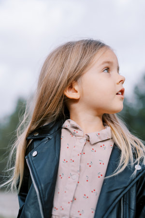 Little girl stands in the park with her head turned to the side. Portrait