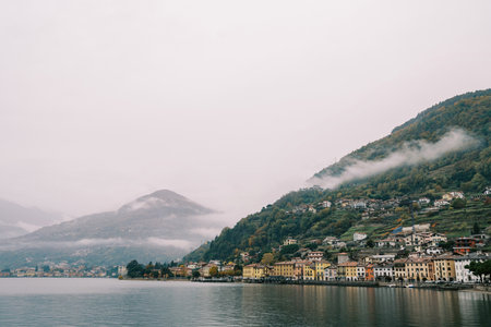 Colorful villas at the foot of forested mountains in the fog on the shores of Lake Como. Italyの写真素材
