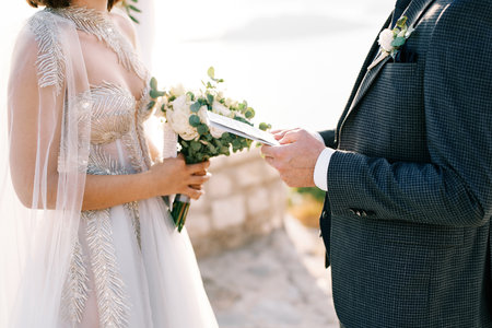 Groom reads an oath to bride from a sheet of paper at the wedding arch. Cropped. Facelessの写真素材