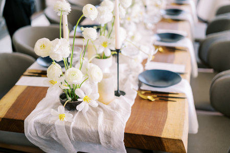 Bouquets of white flowers stand on a narrow fabric on a festive table with black platesの写真素材
