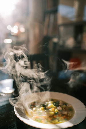 Vegetable soup steams in a white plate on the kitchen tableの写真素材
