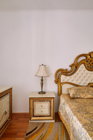 Bronze lamp with a shade on a nightstand next to a Victorian-style double bed
