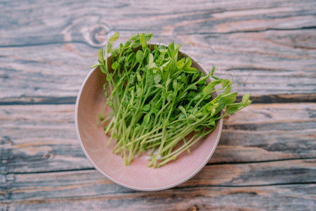 Green pea microgreens lie in a deep plate on a wooden table. Top viewの写真素材