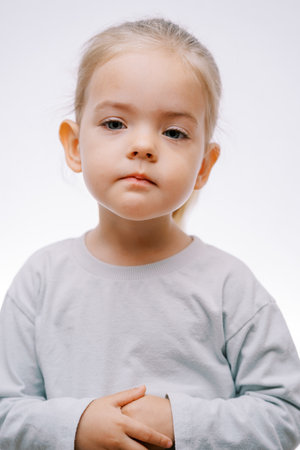 Portrait of a little serious girl with her hands folded on her stomach on a gray backgroundの写真素材