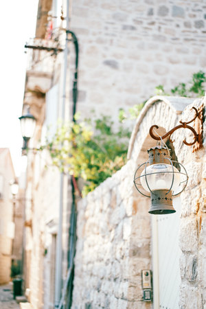 Round antique lantern hangs on a hook on the stone fence of an old houseの写真素材