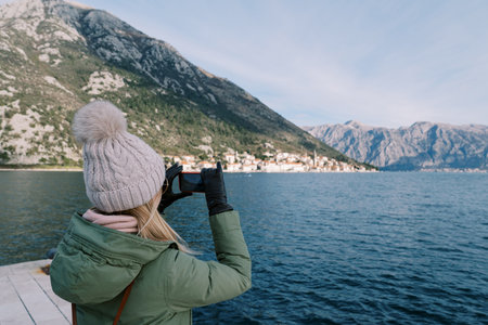 Traveler shoots a mountain range with a smartphone while standing on the pier. Back viewの写真素材
