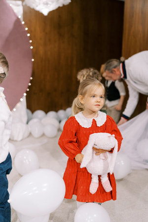 Little girl with a toy rabbit in her hands stands among white balloons on stageの写真素材