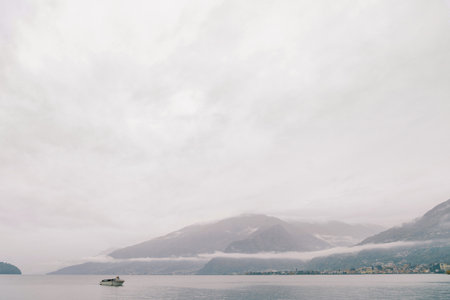 Motorboat sails on Lake Como along a mountain ridge in the fog. Italyの写真素材