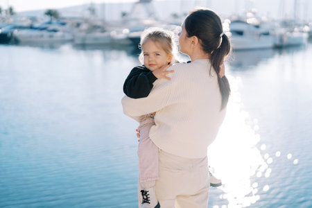Smiling little girl hugging her mother standing on the seashoreの写真素材