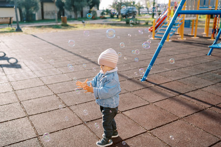 Little girl stands on the playground and tries to catch soap bubblesの写真素材