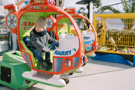 Little girl sits at the helm of a toy helicopter on the playground and looks awayの写真素材