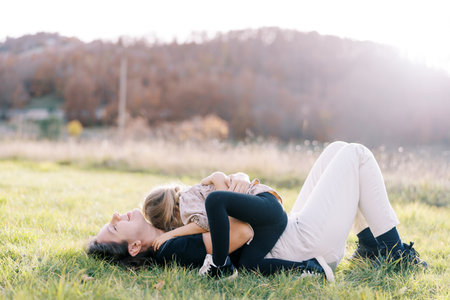 Smiling mother hugging little girl lying on green lawnの写真素材