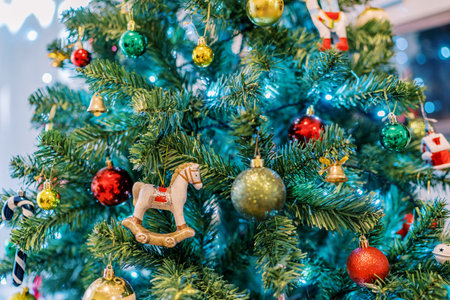 Figurine of a horse on runners hangs among gold, red and green balls on a Christmas tree