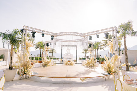 Round stage decorated with bouquets of flowers with spotlights on stands in an open areaの写真素材