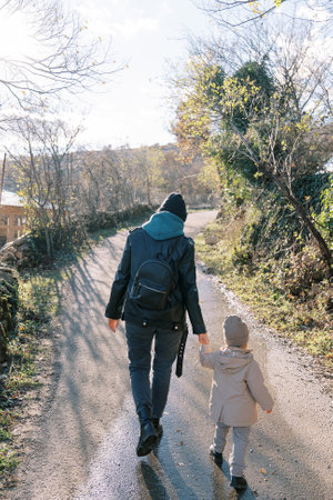 Mother and a little girl are walking along a country road, holding hands. Back view