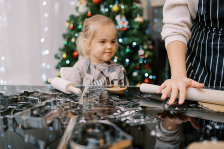 Smiling little girl looks at her mother rolling out gingerbread dough. Croppedの写真素材