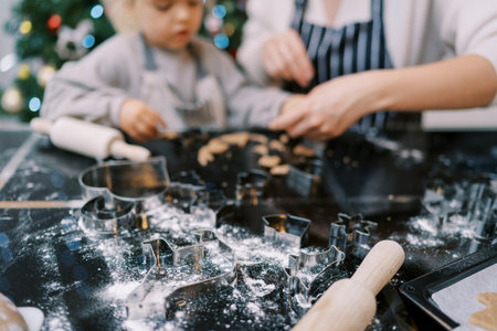 Metal cookie cutters lie on a floured table next to a mother and a little girl kneading dough. High quality photoの写真素材