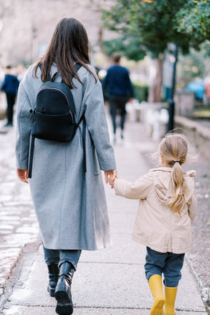 Mother and little girl are walking down the street, holding hands. Back view.の写真素材