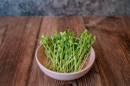 Green sprouts of microgreen peas lie in a plate on a wooden table. High quality photoの写真素材