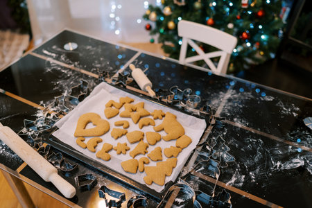 Tray with baked gingerbread cookies stands on a table near a decorated Christmas tree. High quality...