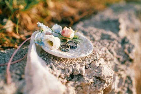 Pair of wedding rings with flowers lie on a saucer on a rock. High quality photo