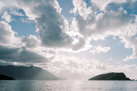 Sun rays shine through the cloudy sky on the mountains in the sea. High quality photoの写真素材