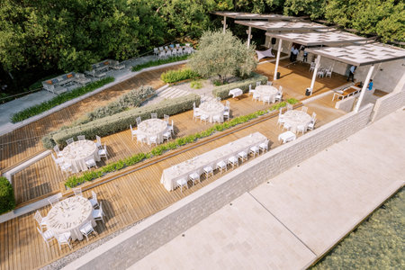Festive tables and chairs are set on wooden floors in the courtyard of the villa. Drone. High...