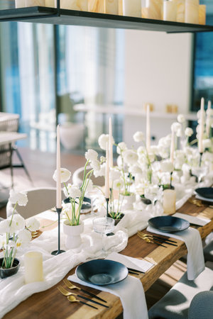 Candles stand near white flowers on a narrow fabric on a festive table with black plates. High quality photoの写真素材