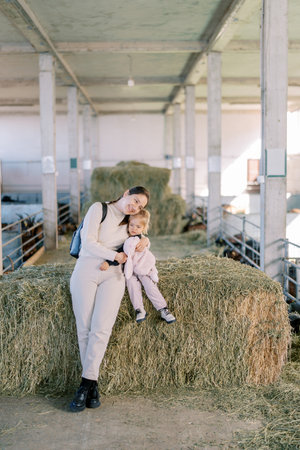 Mom hugs a little girl sitting on a haystack on a farm. High quality photoの写真素材