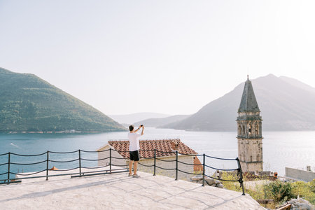 Man on the observation deck takes pictures of the old bell tower. Perast, Montenegro. Back view....