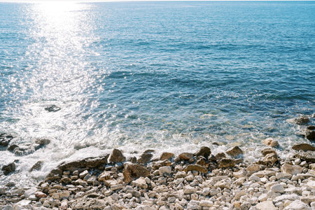 Sea waves sparkling in the sun roll onto the rocky shore. High quality photoの写真素材