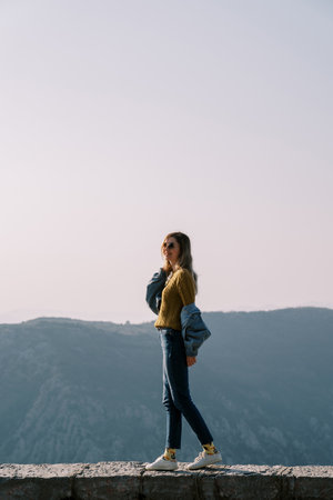 Smiling girl walking along a stone fence high in the mountainsの写真素材