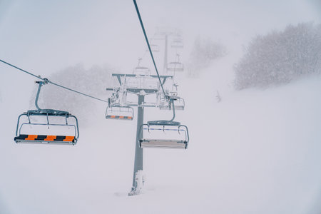 Quadruple chairlift rises above snowy forest to misty mountainの写真素材