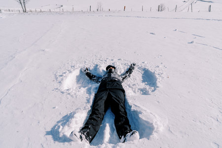 Girl in a ski suit makes a snow angel while lying on the snow