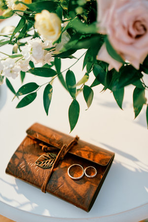 Wedding rings lie on a notepad on the table near the brides bouquet