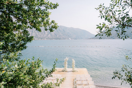 Rows of white chairs stand in front of a wedding arch on a pier by the seaの写真素材