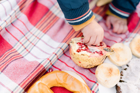 Small child picks out seeds from a pomegranate while sitting on a bedspread. Cropped. Facelessの写真素材