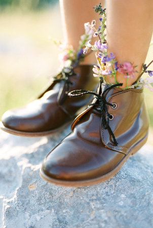 Legs of a little girl in shoes with wildflowers on a stone. Cropped