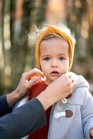 Mom fixes the headband on the little girl head. Portrait. Cropped