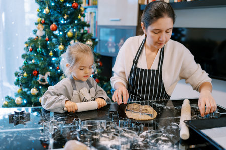 Little girl looking at dough next to mom choosing cookie cutters on tableの写真素材