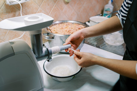 Housewife puts sausage on an attachment on an electric meat grinderの写真素材