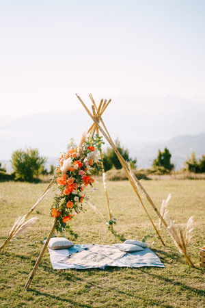 Boho-style wedding arch stands on a green lawn above a bedspread with pillowsの写真素材